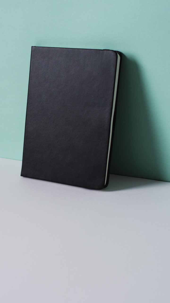 Vertical video of closed black book leaning on wall with copy space in slow motion