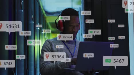 animación de iconos de redes sociales sobre un ingeniero afroamericano usando una computadora portátil en la sala del servidor
