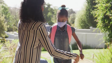 African-american-girl-wearing-face-mask-hugging-her-mother-outdoors-on-a-bright-sunny-day