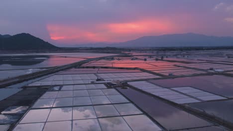 Drone-flying-over-vast-salt-fields-spread-amidst-mountains-during-golden-hour-in-Phan-Rang,-Vietnam