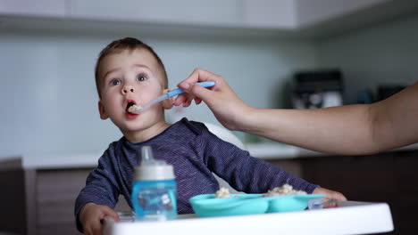 little child looks attentively up while mom feeds him. baby eating porridge and avoids the next spoon.