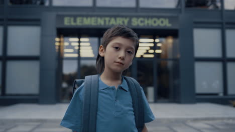 Portrait-pensive-teen-pupil-in-front-modern-school-entrance.-Boy-posing-outdoors