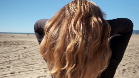 young blonde woman fixing and patting her hair, on the beach volleyball court of santa monica