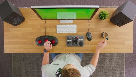 overhead view of male video editor working at computer with green screen in creative office