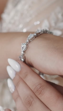 stylish woman bride in wedding dress puts silver bracelet with gems on wrist in room closeup slow motion. accessories for marriage ceremony