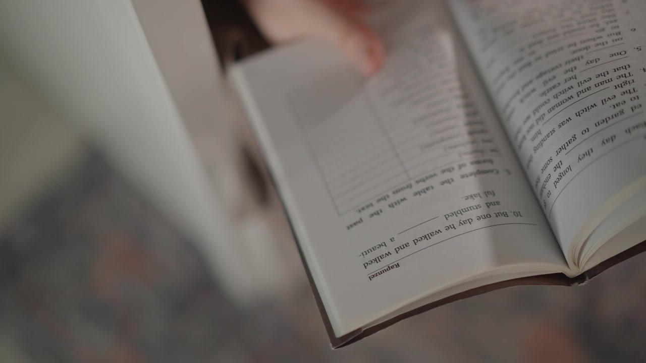 Angled close-up of open notebook with fingers flipping pages, showing printed lines, handwritten notes, lifted paper curl, and gentle motion blur in soft warm light with shallow focus