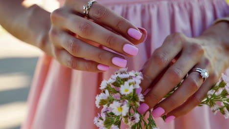 woman's hands with pink nails and rings holding small flowers