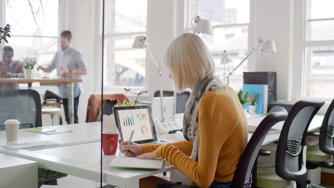 Young business woman working at shared desk in trendy hipster start up office using big data on laptop computer