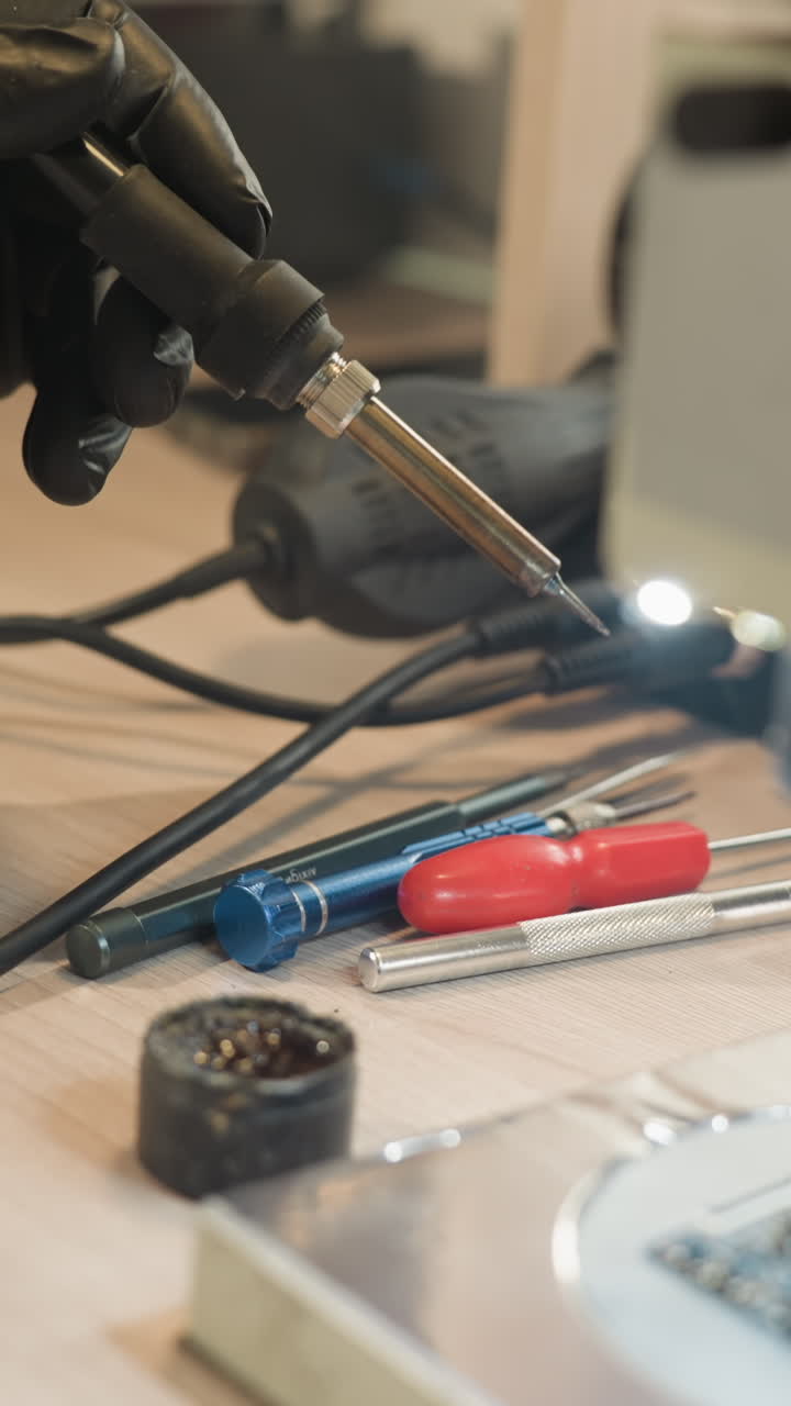 una vista de cerca de la mano con guantes de un técnico sosteniendo un soldador, trabajando en una placa de circuito bajo un microscopio