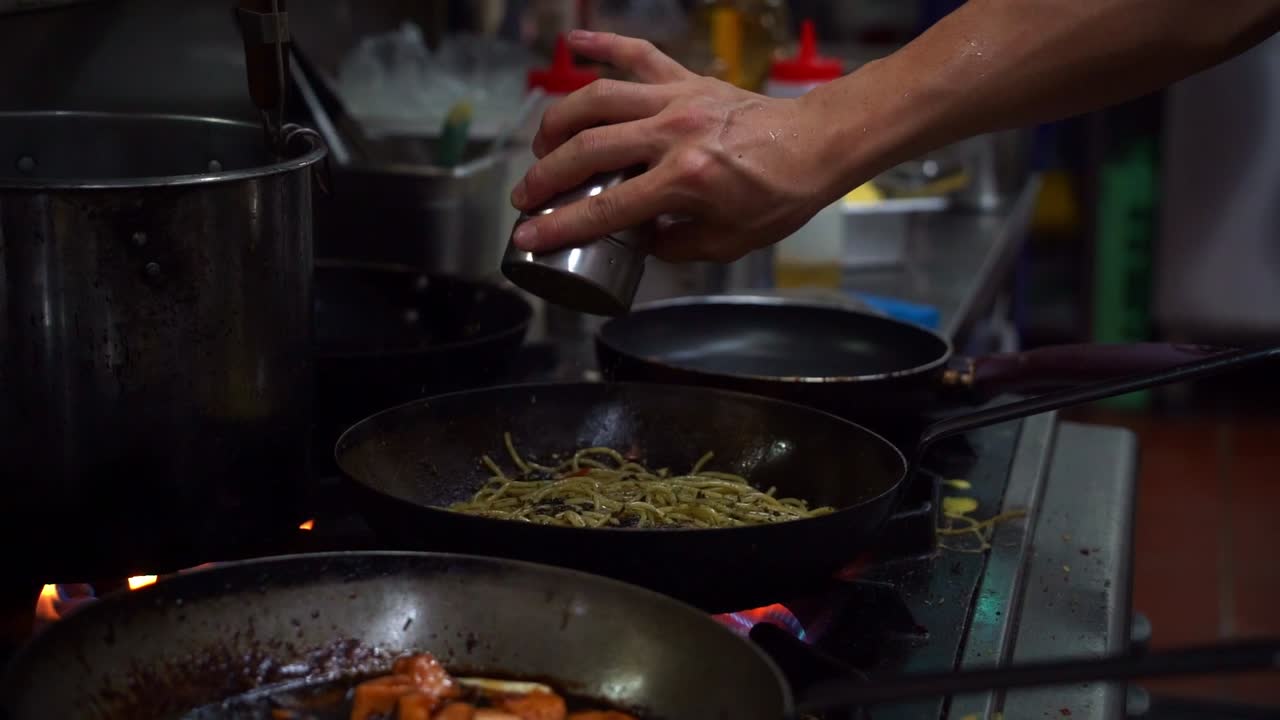 Slow motion shot capturing chef cooking spaghetti aglio olio pasta with sliced bell peppers and bacon, seasoning the ingredients in the frying pan on stovetop