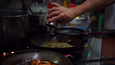 Slow-motion-shot-capturing-chef-cooking-spaghetti-aglio-olio-pasta-with-sliced-bell-peppers-and-bacon,-seasoning-the-ingredients-in-the-frying-pan-on-stovetop