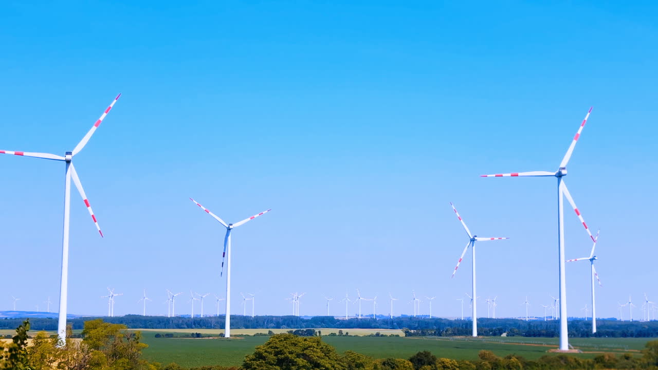 晴れた風景の中で風力タービンが回転しています。澄み切った青空の下、畑の中で風力タービンが回っています。地平線まで広がる畑は、クリーンなエネルギー生産を示しています。