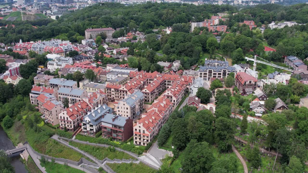 Immagine aerea realizzata con drone sopra il distretto di Markučiai, Vilnius, Lituania, che mostra case con tetti rossi, un'ansa del fiume e una fitta vegetazione in una luminosa giornata estiva