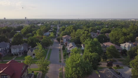 Drone-Moviéndose-Hacia-Atrás-Y-Captura-El-Camino-De-Los-Suburbios-Con-Residencia-Múltiple-En-El-Lateral-Y-árboles-Verdes