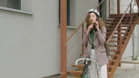 pretty curly woman in formal clothes wearing a bicycle helmet in the city