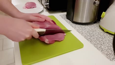 Caucasian-woman-cutting-up-pork-meat-with-a-white-knife-on-a-green-board