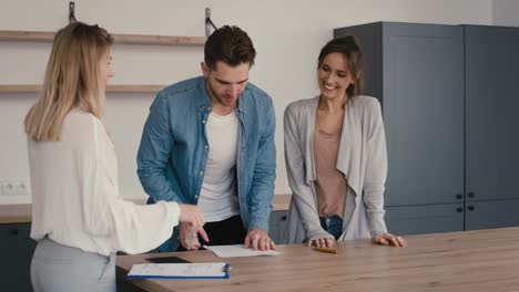 una joven pareja caucásica firma un acuerdo de compra de casa con un agente inmobiliario.