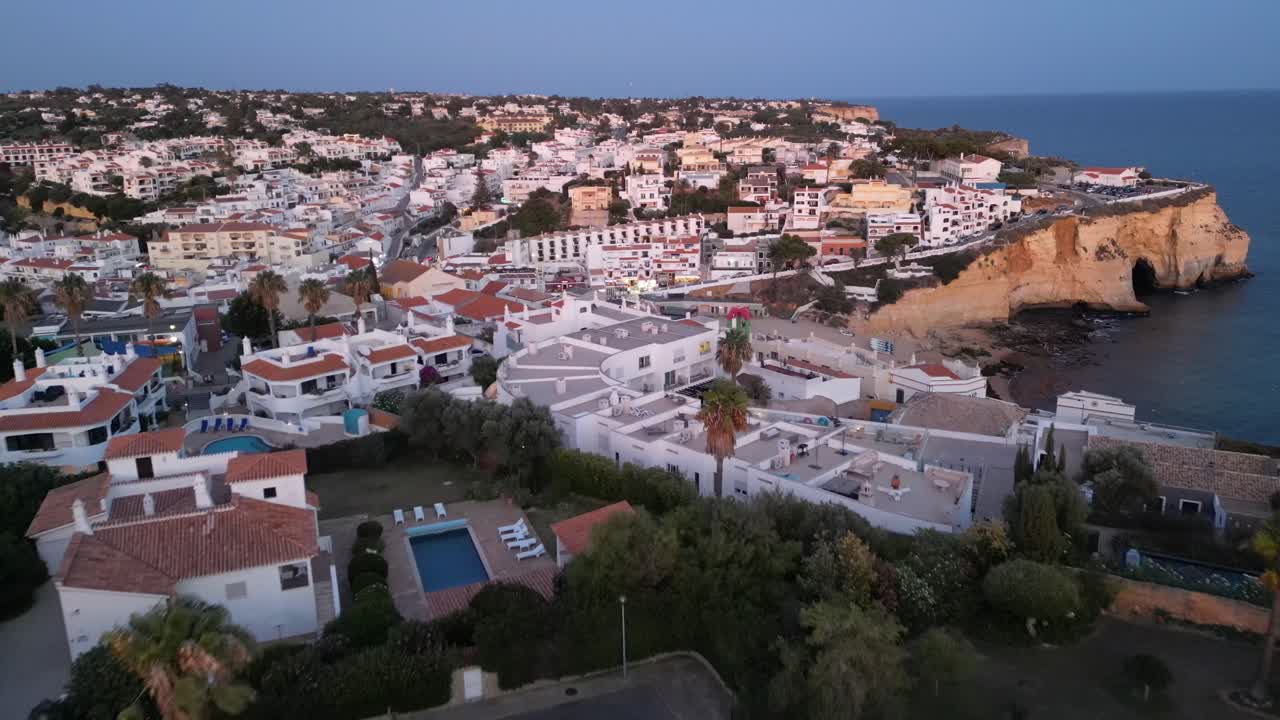 해가 지는 동안 카르보에로 위를 날아다니는 드론의 항공기, 절벽이 보이고  마을의 집과 해변이