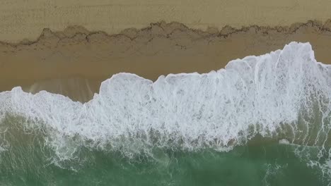 aerial top-down view of waves breaking on sandy beach