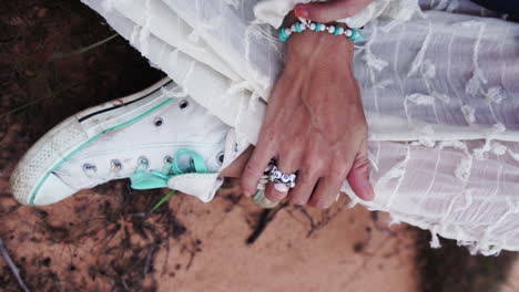 closeup view of female hands as they run over white shoes, sitting on the grass and wearing a white dress