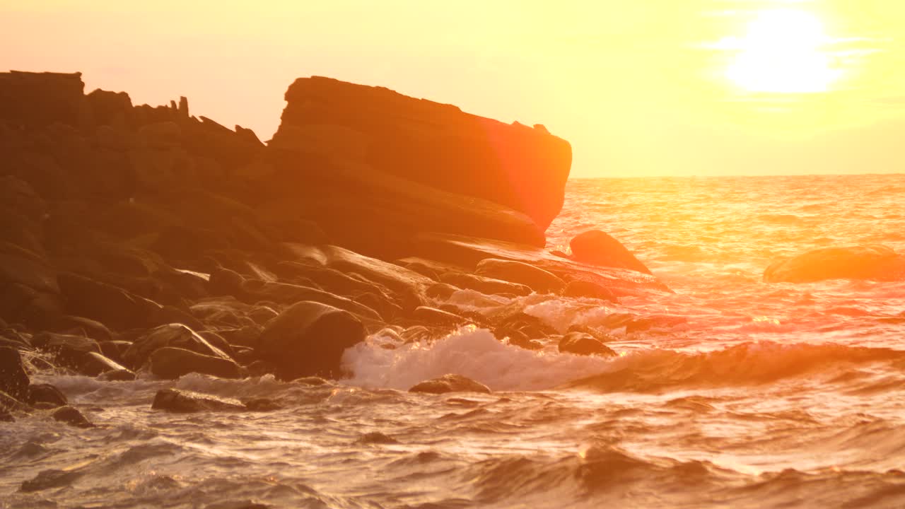 Sunset sun setting, ocean waves over shore stones cliff in Southeast Asia