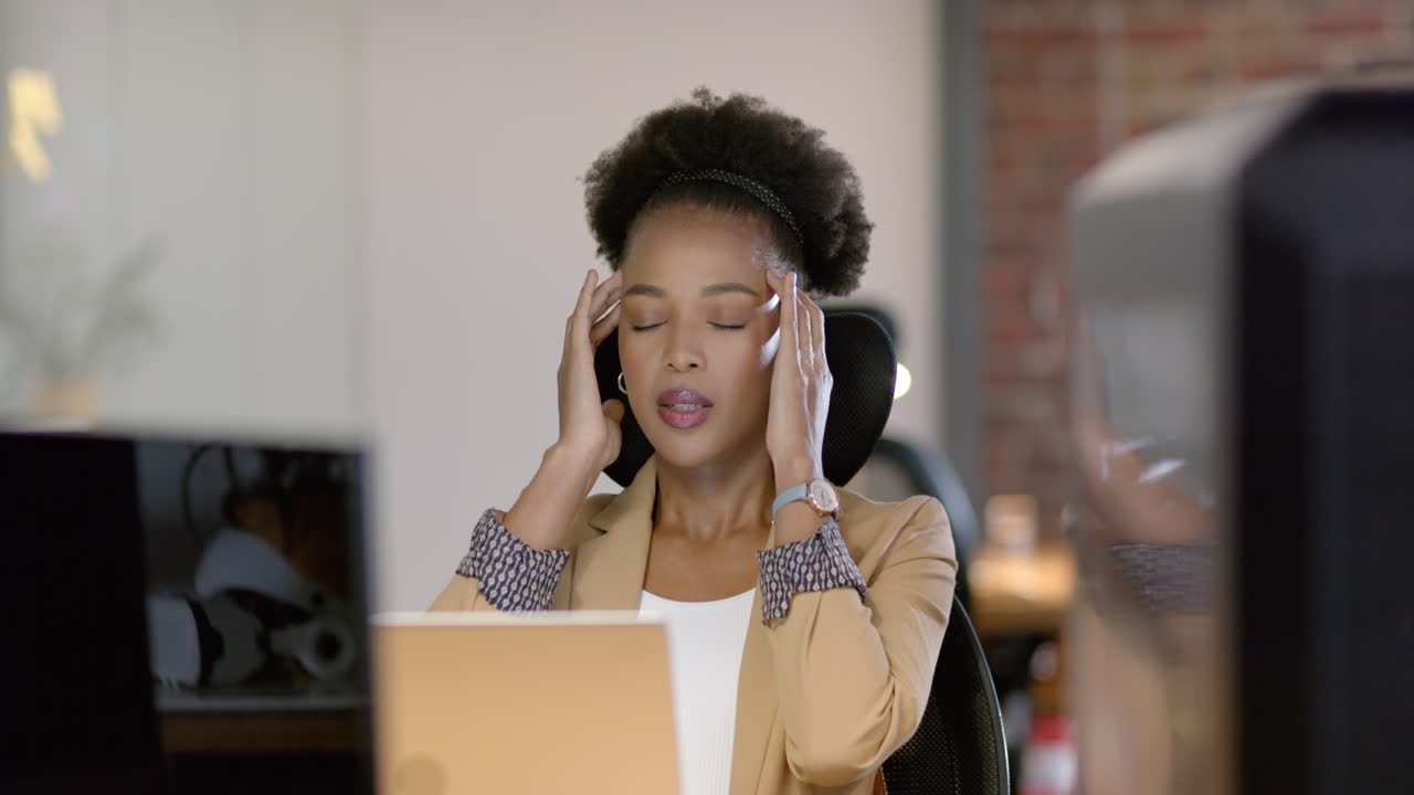 A young African American woman looks stressed at her business office desk