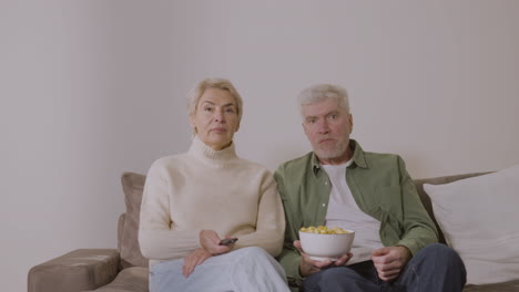 senior couple talking and watching tv while sitting on sofa at home