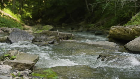 Mittlere-Zeitlupenansicht-Des-Wassers,-Das-Mit-Großen-Felsblöcken-Einen-Breiten-Bach-Hinunterfließt