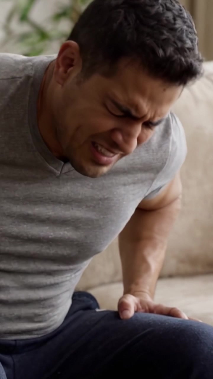A Man Confronts His Discomfort: Physical Struggle and Emotional Turmoil during a Moment of Pain and Reflection while Sitting on a Couch