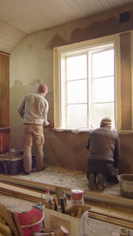 slider shot of two men plastering walls with clay, home improvement, vertical