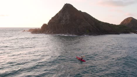 aerial drone circling view of man in red kayak paddling toward na mokulua hawaiian islands off windward coast of oahu, hawaii