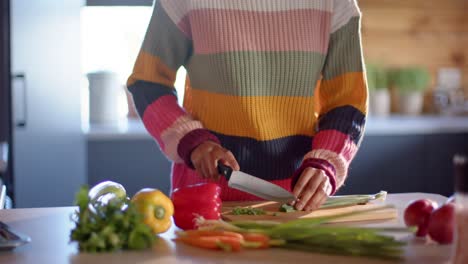 mujer afroamericana cortando verduras en la cocina soleada