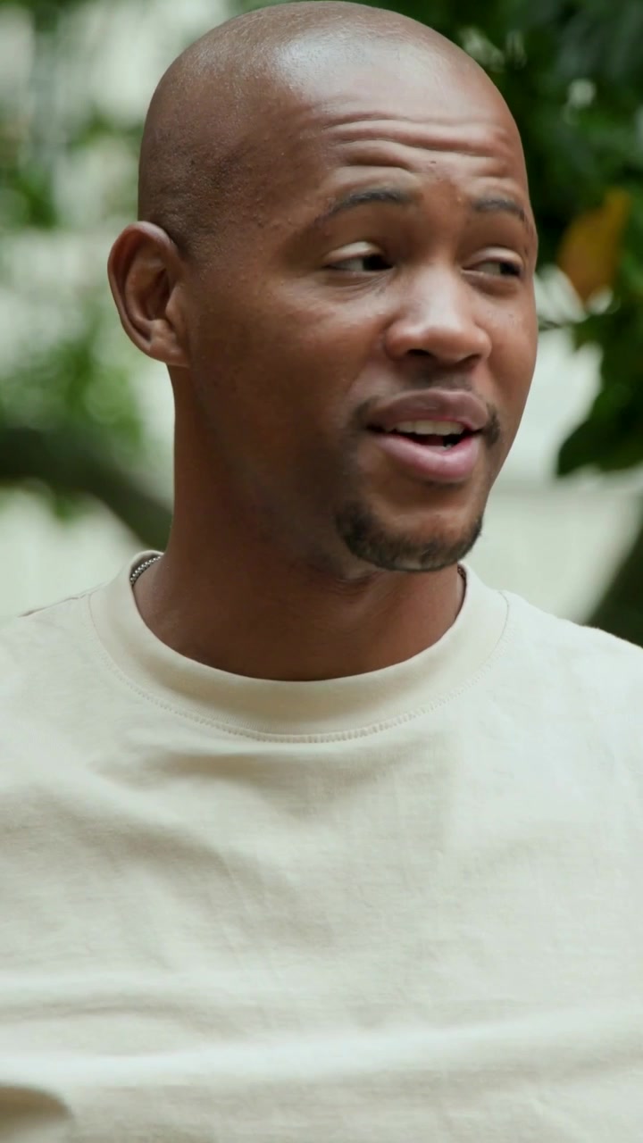 Vertical video: Panning cam man in beige tee speaking briefly turning at yard with tree, copy space
