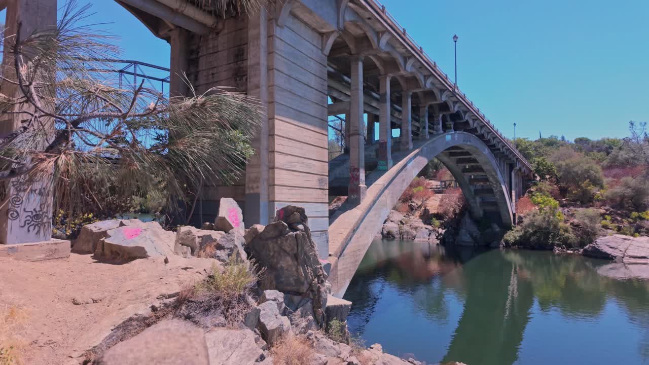 A cinematic panning shot of the Folsom Historic Truss Bridge in California. The steel structure spans the American River