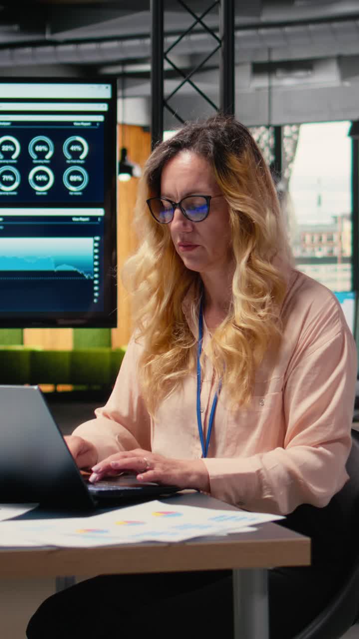 Vertical Video Businesswoman at her desk on analytics displayed with her laptop
