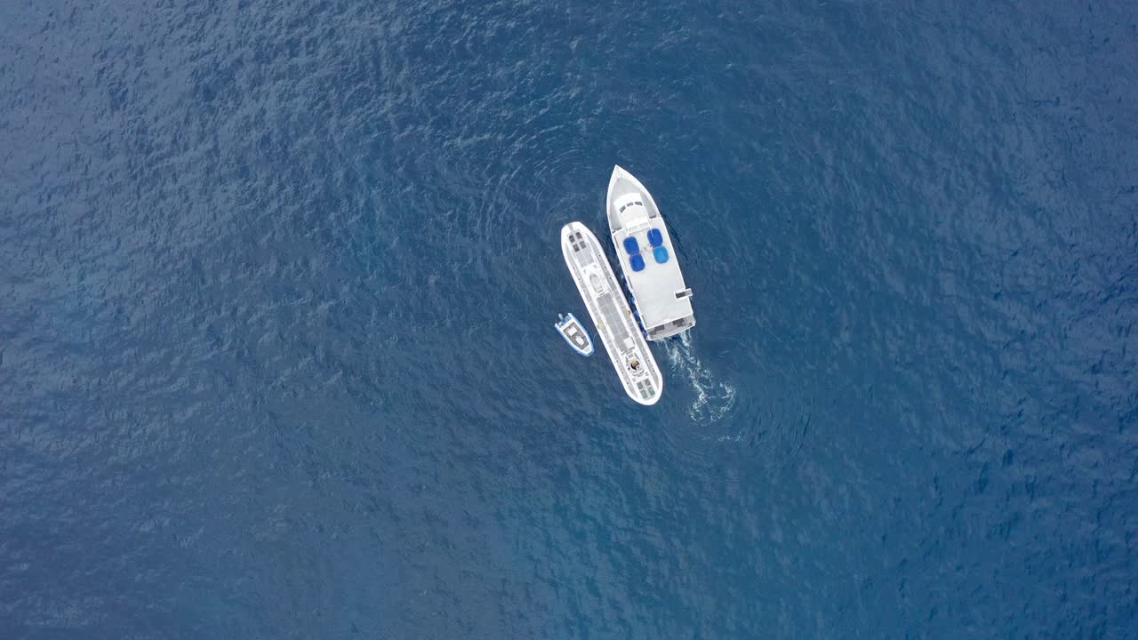 Wide aerial bird's eye shot looking down at a submarine in the open ocean as a small ferry boat pulls away in Hawai'i