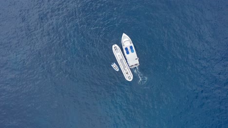 Wide-aerial-bird's-eye-shot-looking-down-at-a-submarine-in-the-open-ocean-as-a-small-ferry-boat-pulls-away-in-Hawai'i