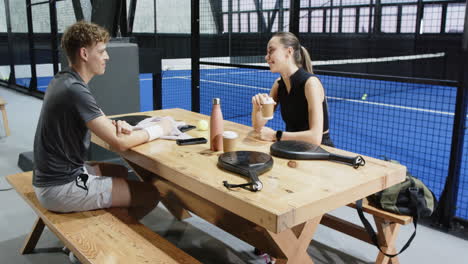 young athletes discussing strategy at padel tennis court, holding rackets and drinks