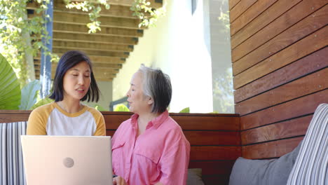 using laptop, young asian woman talking with senior asian woman on wooden bench