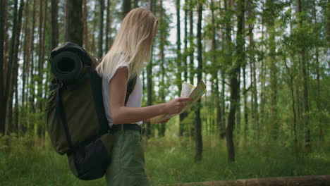 A-young-woman-with-a-map-is-walking-through-the-forest-traveling-with-a-backpack-in-slow-motion.-Traveler-in-shorts-in-the-woods