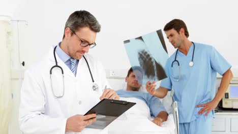 Doctor-checking-sick-patients-chart-while-surgeon-looks-at-xray