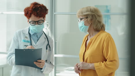 mujer médico y mujer mayor con máscaras hablando en la clínica