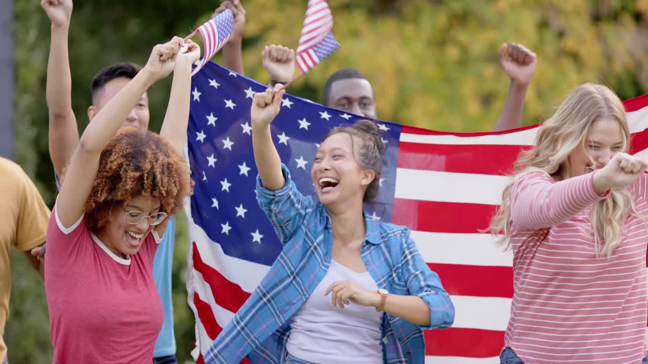 Happy diverse group of friends holding flags of usa and celebarting in garden, slow motion