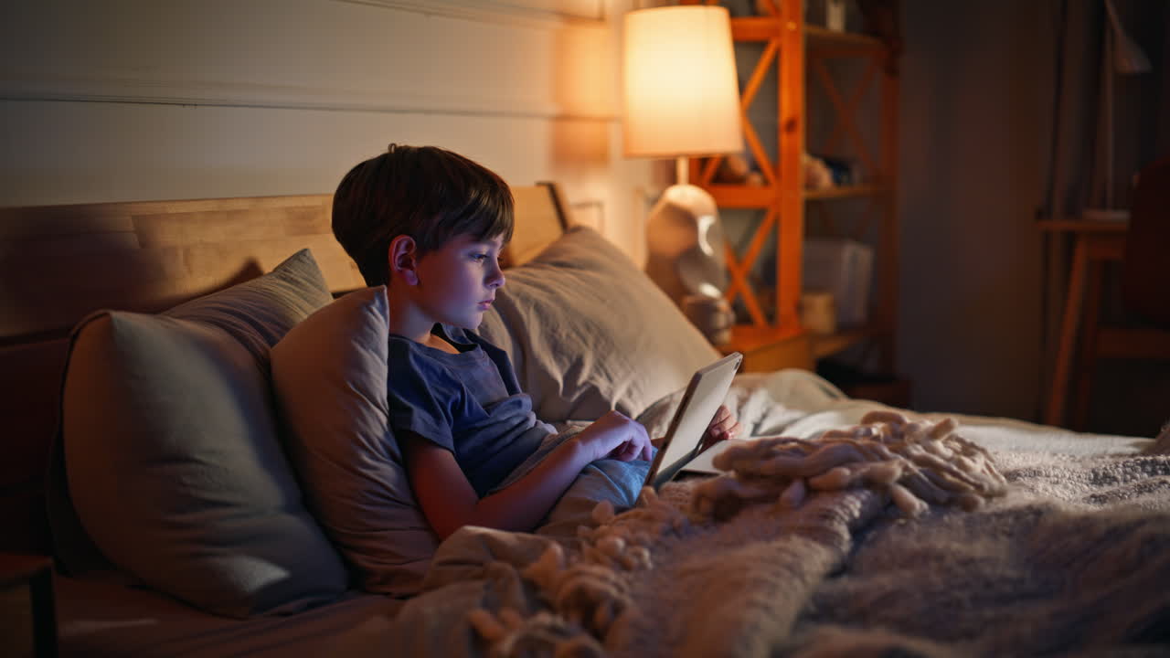 Little boy using tablet at bedtime lying home bed closeup. Kid browsing content