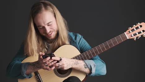 Joven-Caucásico-Con-Guitarra-Usando-Su-Teléfono-Inteligente-En-La-Cámara.