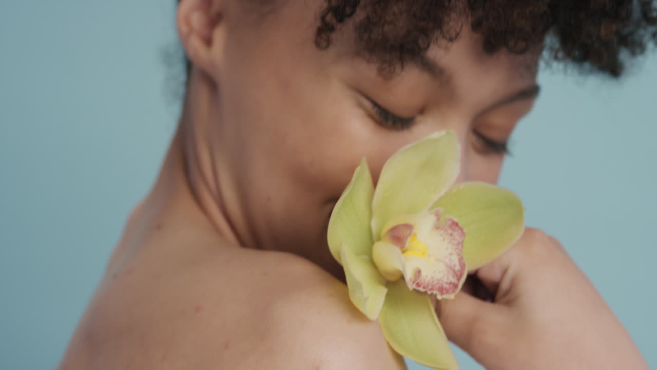 close up portrait beautiful young woman touching skin with orchid flower caressing smooth healthy complexion enjoying natural beauty fragrance on blue background skincare concept
