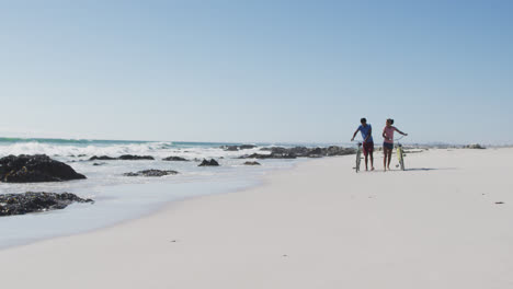 una pareja afroamericana caminando con bicicletas en la playa