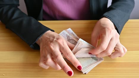 high angle view of an accountant woman with red fingernails counting thai baht banknotes on wooden table.