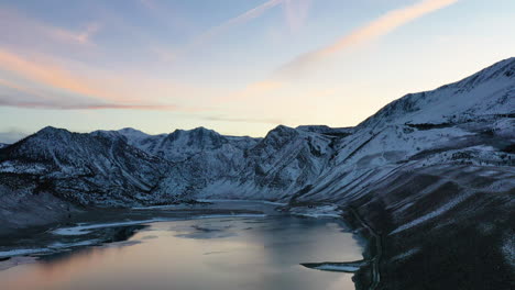 sunlight reflection on lake water with majestic mountain range in background, aerial ascend view