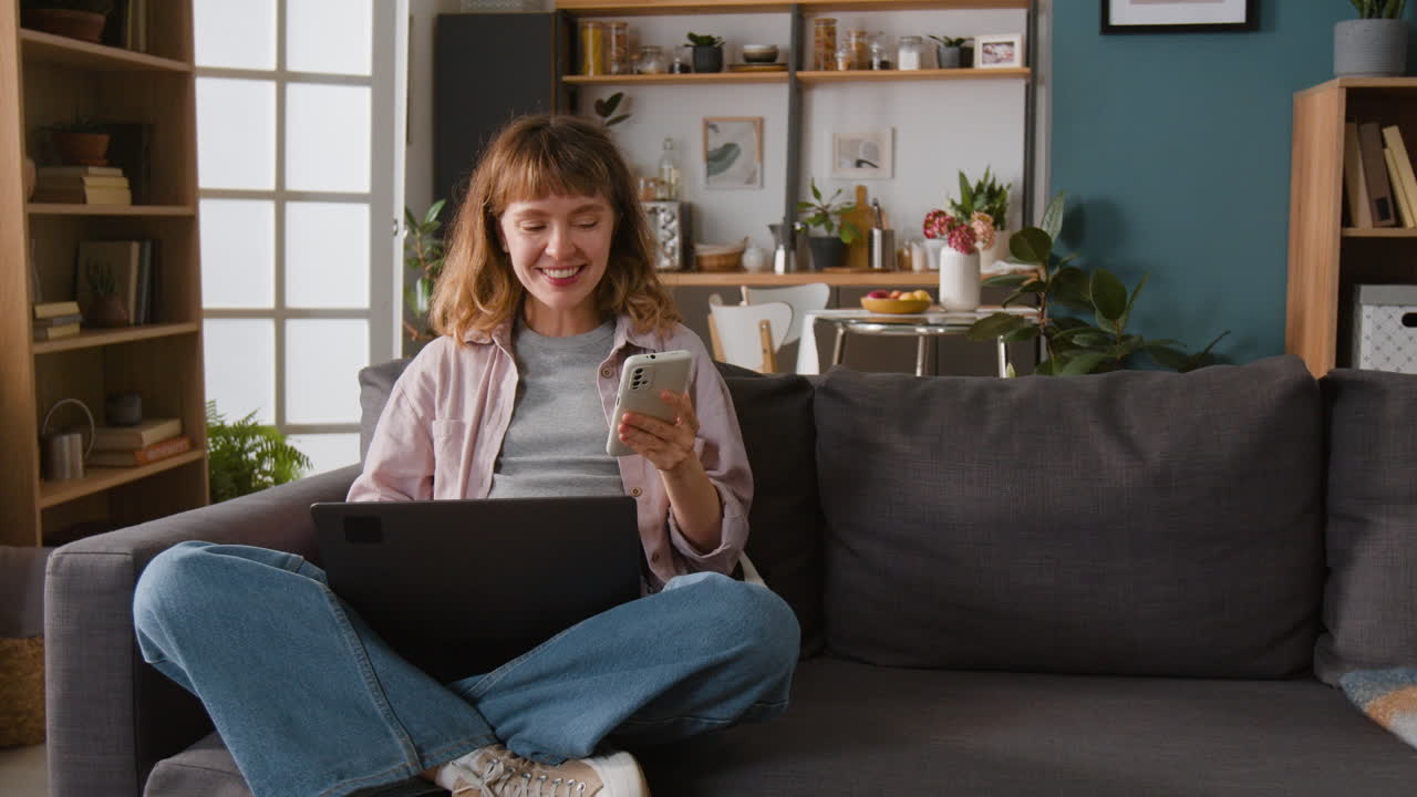 Woman using laptop and smartphone on couch at home